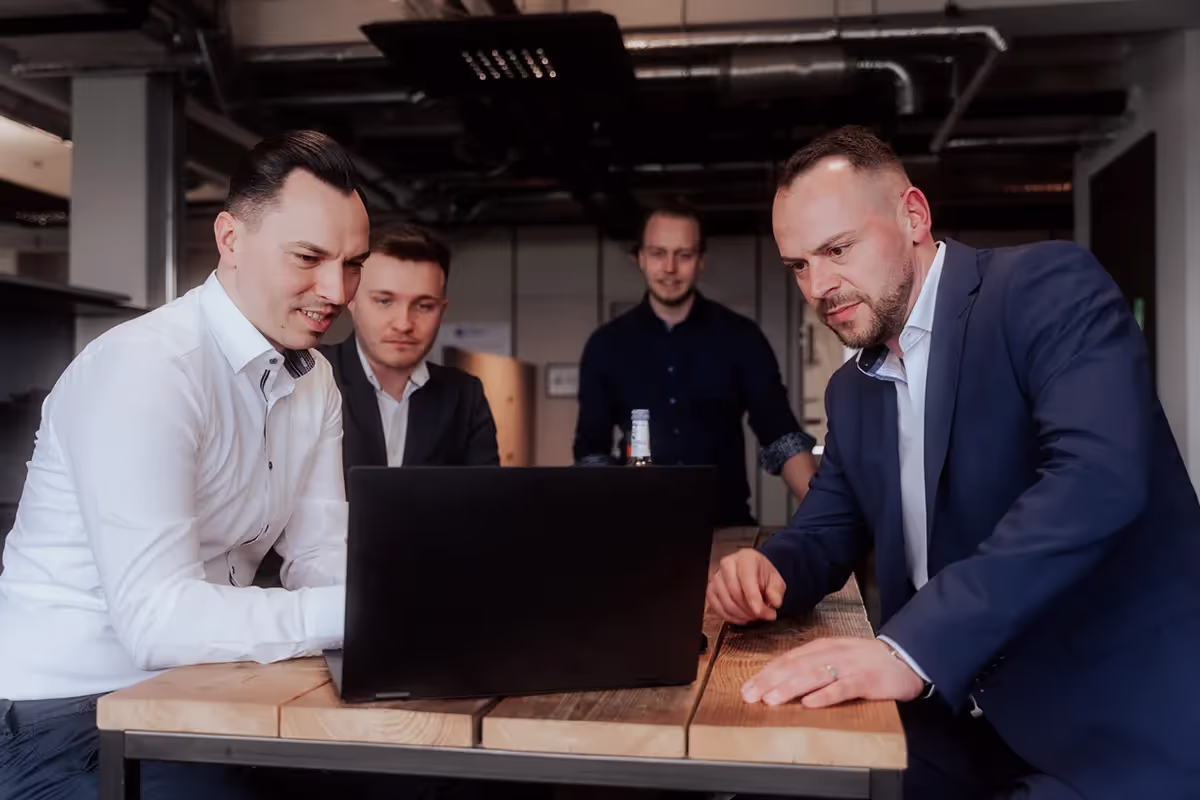 Vier Männer sitzen vor einem Laptop und schauen sich etwas an.