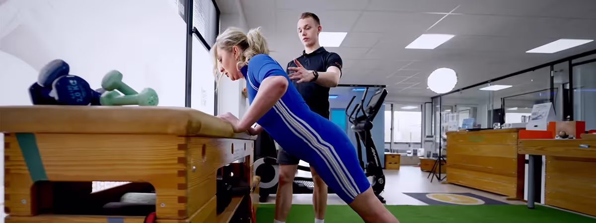 Ein Personaltrainer neben einer Frau, die gerade eine Übung macht.