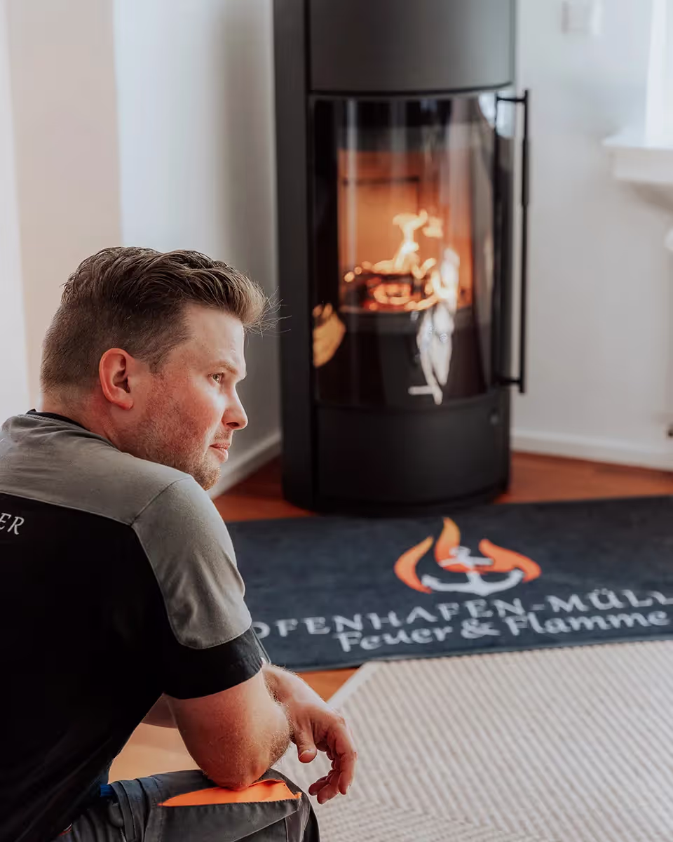 Ein Mann sitzt vor einem Kamin, in dem Feuer brennt.