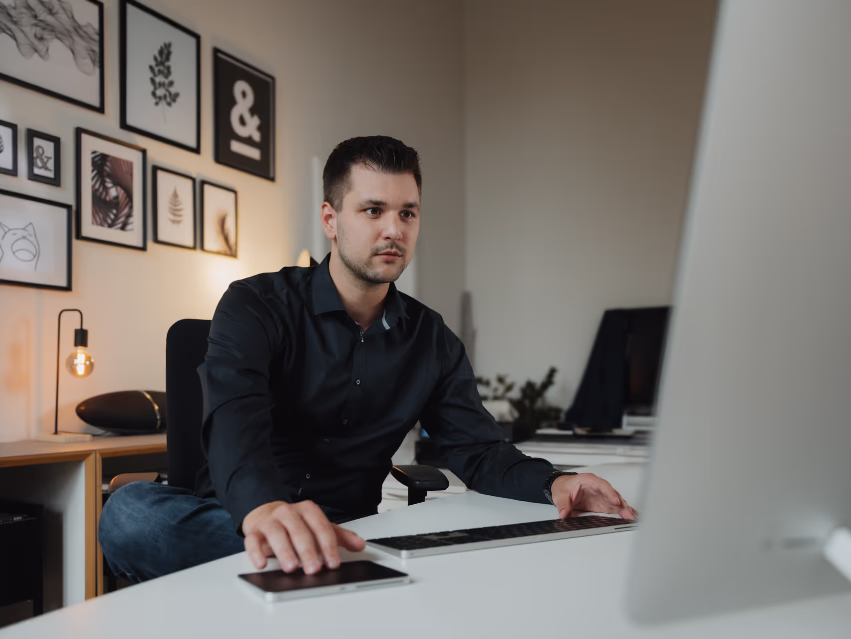 Mann mit dunklem Hemd sitzt an einem Schreibtisch und arbeitet konzentriert am Computer.